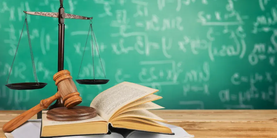 Gavel on books on a desk with scales and chalkboard in background